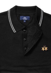 Svart pikétröja i stickat tyg med treknappsprydd halsspalt, randig krage och en guldembroderad logotyp med två hästar.