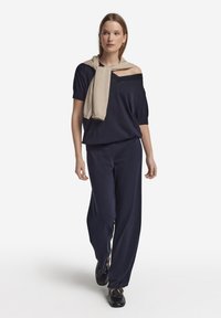 Marinblå tvådelad outfit med en lös off-shoulder topp med korta ärmar och vida byxor, accentuerad med en ljusbeige stickad scarf.