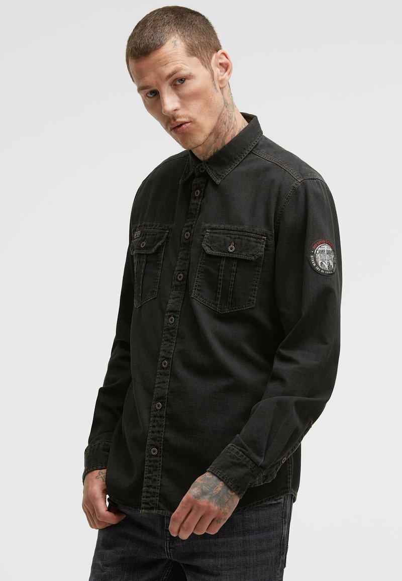 Schwarze Denim-Button-Down-Bluse mit zwei Brusttaschen, kontrastierenden Nähten und einem runden Aufnäher am linken Ärmel. Langärmliges Design mit Kragen.