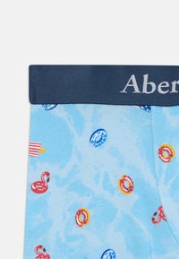 Blå boxershorts med et marineblått elastisk belte, prydet med et lekent mønster av flamingoer og svømmeringer på en lyseblå bakgrunn.