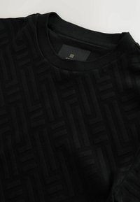 Sort crew-neck T-shirt med et struktureret mønster af geometriske former. Lavet af blødt stof med en glat overflade.