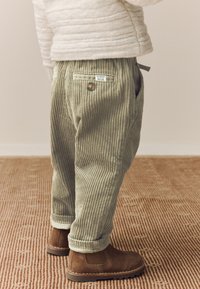 Pantalon en velours côtelé vert olive clair, avec des côtes verticales, une taille ajustable, une fermeture à bouton unique et des poches.