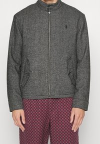 Šedý saka s rybím vzorem, stojáčkovým límcem, předním zipem, dvěma bočními kapsami a černými švovými detaily; kombinováno s vzorovanými vínovými kalhotami.