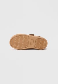 Schuhsohle aus strukturiertem braunem Gummi, mit einem Zickzackmuster für besseren Halt und einer flachen, abgerundeten Form ohne sichtbare Abnutzung.