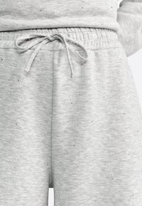 Pantaloni della tuta grigi con una texture morbida, cinturino elastico in vita, cordoncino regolabile e piccoli accenti lucidi disseminati nel tessuto.