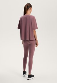 Løs pasform mauve t-shirt parret med matchende leggings. Blødt stof med glat tekstur. Sorte atletiske sko fuldender outfittet.
