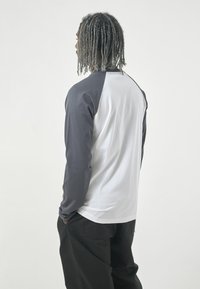 Langarmshirt mit weißem Körper und dunkelgrauen Raglanärmeln, aus weichem Material gefertigt. Einfaches Design mit rundem Ausschnitt und lässiger Passform.