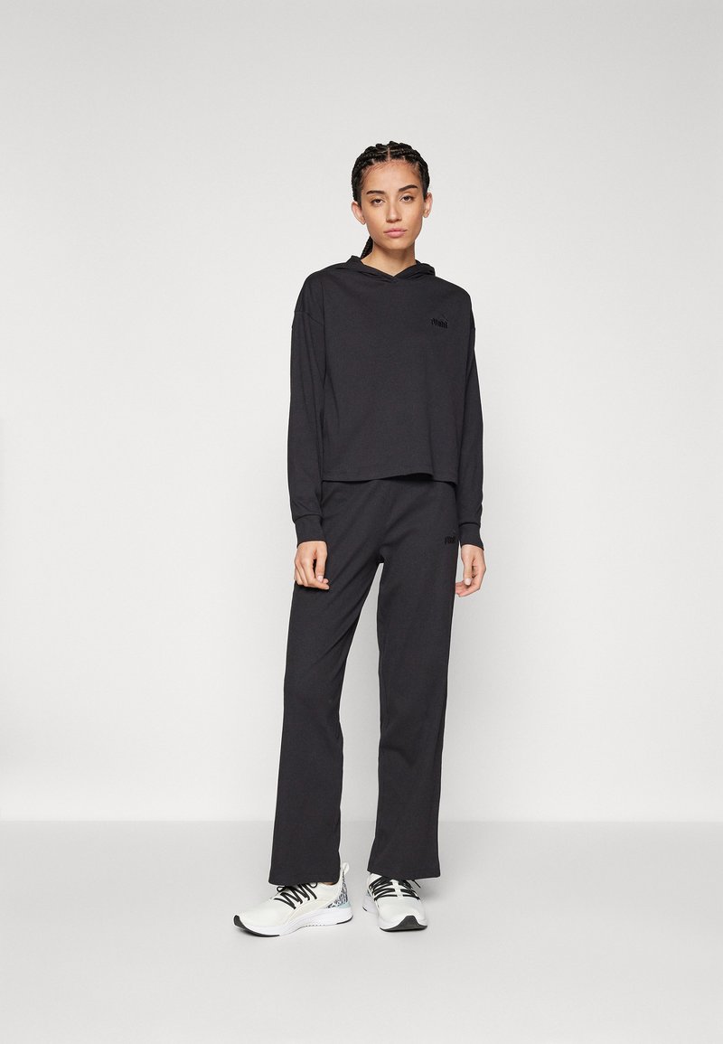 Felpa nera corta con maniche lunghe e pantaloni coordinati di taglio morbido. Il materiale sembra soffice; include dettagli con il logo. Indossata con scarpe da ginnastica bianche.