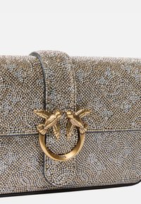 Borsa a mano con perline d'oro e d'argento con superficie texturizzata, caratterizzata da un elemento decorativo a forma di uccello circolare come chiusura. Design rettangolare elegante.