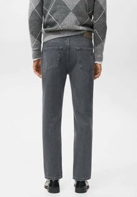 Vaqueros de denim gris con un corte recto, que presentan un diseño clásico de cinco bolsillos y costuras visibles. Llevados con un suéter gris con estampado.