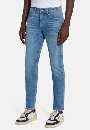 Jean en denim bleu clair avec une coupe droite, texture délavée, design à cinq poches et fermeture à bouton en métal, associé à des baskets.