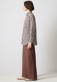 Chemise à rayures marron et crème à boutonnières avec une poche poitrine ; assortie avec un pantalon large marron et des baskets de couleur claire.