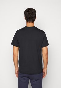 Czarna bawełniana koszulka z krótkim rękawem, okrągłym dekoltem i prostym wzorem; wyeksponowana z tyłu na neutralnym tle.