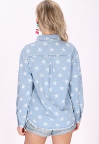 Világoskék farmering csillagmintával, hosszú ujjakkal és laza fazonnal. A hátsó részen gombos dizájn és redő részletek találhatóak.