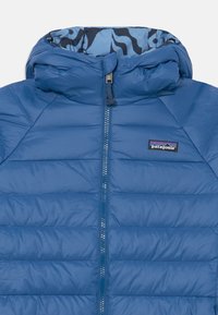 Veste rembourrée bleue avec capuche, dotée d'un rembourrage matelassé, d'une fermeture éclair à l'avant et d'une doublure intérieure avec un motif zèbre. Logo Patagonia affiché.