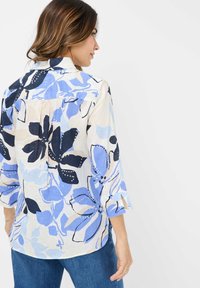 Lightweight, patterned blouse in light cream with blue and navy floral designs. Features a collar and three-quarter sleeves with slit cuffs.