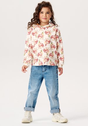 Lichte crème hoodie met een bloemenpatroon in roze en groen, gecombineerd met losse, lichtblauwe denimjeans en witte sneakers.