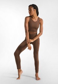 Completo activewear marrone composto da un crop top aderente e leggings a vita alta. Il tessuto è liscio con cuciture piatte e una vestibilità aderente.