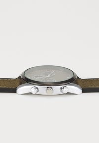 Montre chronographe avec un boîtier rond noir, un bracelet en cuir texturé vert foncé, des finitions en acier inoxydable argenté et un cadran noir détaillé avec des sous-cadrans.