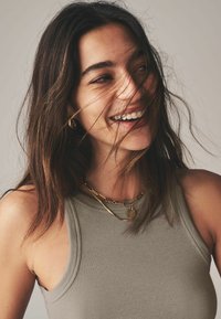 Halli halliga tank top, millel on sobiv disain, kihilise kuldse ketiga kaelakeed ja lahtine tume juuksehood, mille väljajäävad harud katavad osaliselt nägu.