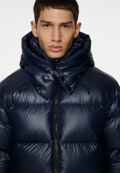 Navy puffer jacket with a high, structured collar, featuring a zip closure and snap buttons. Glossy finish with horizontal quilted design.