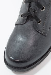 Šedá kožená kotníková bota s hladkým povrchem, texturovaným svrškem, kulatou špičkou a kovovými očky na tkaničky. Gumová podrážka je viditelná podél okraje.