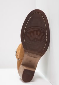 Hnědá semišová bota s texturovanou podrážkou, koženým podpatkem a kovovými detaily; logo "SHABBIES" a velikost "37" je vytlačeno na podrážce.