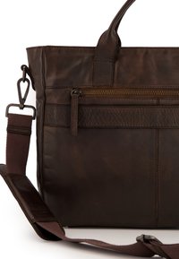 Sac fourre-tout en cuir marron foncé avec une finition texturée, équipé de poignées supérieures, d'une sangle amovible et d'une poche avant zippée.