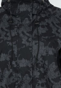 Svart jacka med ett hexagonalt mönster och en slät textur, justerbara snörning och en kamouflage-design i olika nyanser av grått.