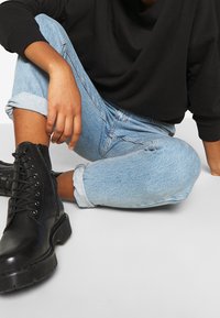 Bottines noires à lacets avec une finition texturée, associées à un jean denim bleu clair retroussé et un haut noir ample.