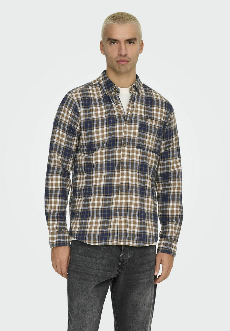 Kariertes Hemd in Blau, Braun und Weiß. Mit einem Button-Down-Kragen und einer einzelnen Brusttasche. getragen mit dunklen Jeans.