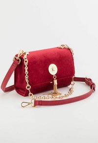 Sac à bandoulière en velours rouge avec des accents en chaîne dorée, doté d'un pompon décoratif et d'une fermeture à pression, de forme rectangulaire, texture lisse.