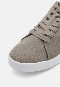 Grey fabric sneaker with white rubber sole, featuring rounded toe, textured upper, and flat laces threaded through metal eyelets.