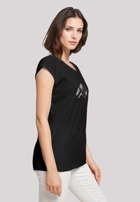 Zwarte t-shirt met korte opgerolde mouwen, voorzien van een zilveren bergafbeelding op de voorkant. De stof lijkt soepel en lichtgewicht.