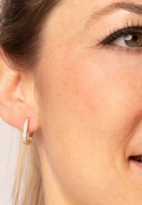 Gold-tone hoop earring with a curved design featuring a row of small clear crystals along one side. Smooth metal finish.