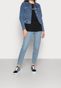 Jeansjacka i medelblå färg med framfickor, ihop med en svart t-shirt och ljusblå jeans. Svarta sneakers med vita snören fulländar utseendet.