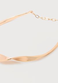 Κολιέ από μέταλλο χρυσού χρώματος με ομαλή, κυρτή σχεδίαση και αλυσίδα κλεισίματος πάνω σε λευκή επιφάνεια.