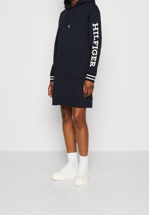 Robe sweat à capuche navy avec le texte blanc "HILFIGER" le long de la manche, poche kangourou et poignets côtelés rayés. Texture douce, design décontracté.