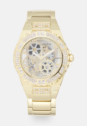 Gold-tone wristwatch with a transparent face displaying gears, surrounded by a crystal-encrusted bezel and a metallic link bracelet.