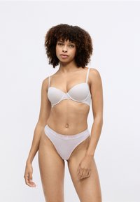 Soutien-gorge gris clair avec bonnets lisses et bretelles réglables, associé à un string taille haute assorti arborant le logo Calvin Klein en rose pâle.