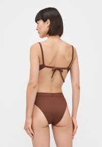Rjav rebrast bikini z nastavljivimi naramnicami in vezanjem na hrbtu. Visok pas na dnu z gladkim zaključkom, ki poudarja minimalističen design.