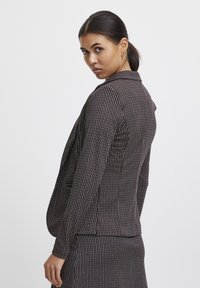 Suknja blazer v črno-beli houndstooth vzorcu, s poševnim ovratnikom, dolgimi rokavi in prilegnjenim silhuetom ter stranskimi žepi.