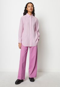 Camicia button-up rosa chiaro con maniche lunghe, orlo arrotondato, abbinata a pantaloni a gamba larga dello stesso colore e scarpe platform nere spesse.