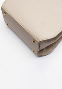 Borsa a tracolla in pelle beige con una forma strutturata, dotata di accessori in tonalità oro e borchie decorative sulla base. Sottile dettaglio del logo in rilievo.