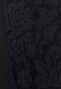 Tissu en dentelle noire avec des motifs floraux sur un fond noir uni, montrant un maillage complexe et des détails texturés.