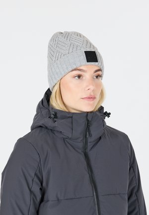 Bonnet en laine grise avec un motif texturé et un patch logo noir, porté sous une doudoune foncée à fermeture éclair.