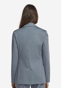 Ljust grå skräddarsydd blazer med en strukturerad design, skarpa kragar och en ventilerad rygg. Slät tyg med en subtil glans.