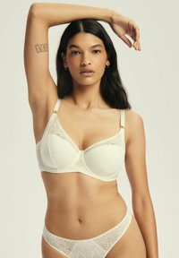 Cream lace bra with underwire, featuring geometric patterns and adjustable straps. Paired with matching lace panties.