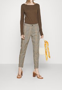 Ruskea pitkähihainen paita yhdistettynä ruutukuosisisiin, korkeavyötäröisiin beigeihin ja mustiin housuihin. Asusteita ovat vaaleanbeige käsilaukku, jossa on keltainen sidottu huivi.