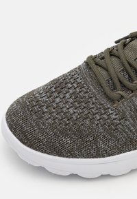 Scarpa sportiva leggera in tessuto a rete grigio oliva. Presenta una tomaia testurizzata, una soletta bianca imbottita e lacci coordinati.